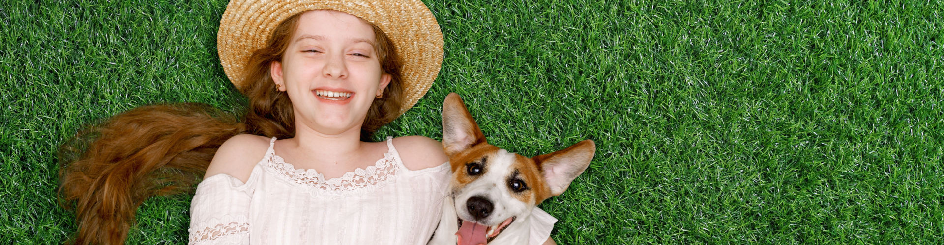 Young girl and her corgi puppy laughing and relaxing together on pet-friendly artificial turf for dogs